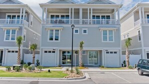 A row of three-story townhouses with balconies, a driveway, and a parked car. - Village West #16, Oceanview Townhouse in Emerald Isle, NC! (Emerald Isle)