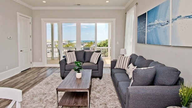 A spacious living room with a gray sofa, a wooden coffee table, and a large window offering a view of the ocean. - Village West #16, Oceanview Townhouse in Emerald Isle, NC! (Emerald Isle)