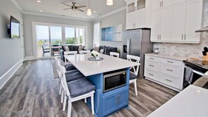 A modern kitchen with a central island, white cabinets, and a view to the outside. - Village West #16, Oceanview Townhouse in Emerald Isle, NC! (Emerald Isle)