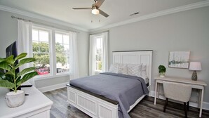 A bedroom with a bed, a desk, a chair, a ceiling fan, and a window with curtains. - Village West #16, Oceanview Townhouse in Emerald Isle, NC! (Emerald Isle)