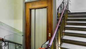 A staircase with a wooden door at the bottom, metal railings, and a glass elevator shaft. - Principe Ludovico - La Dimora degli Affreschi Florence (Florence)