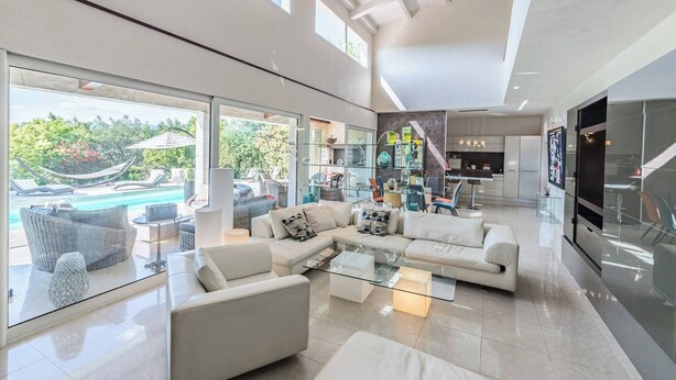 A spacious living room with a large glass door leading to a pool area, a modern kitchen, and a staircase. - DIANE By Terry's Homes (Cannes)