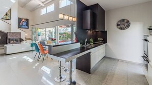 A modern kitchen with a central island, bar stools, and a large window providing natural light. - DIANE By Terry's Homes (Cannes)