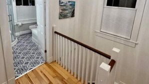 Un corridoio con pavimento in legno, pareti bianche, un termosifone bianco e un lampadario al soffitto.