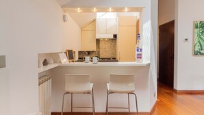 A modern kitchen with a central island, two bar stools, and a view into the dining area.