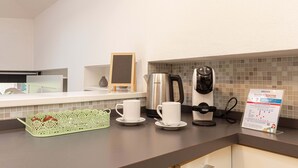 A hotel kitchenette with a coffee maker, two white cups, a kettle, and a sign about a loyalty program.