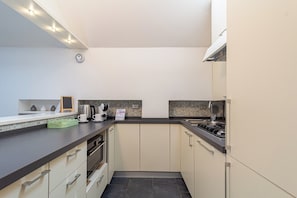 A modern kitchen with a dark countertop, white cabinets, a gas stove, and a coffee maker.
