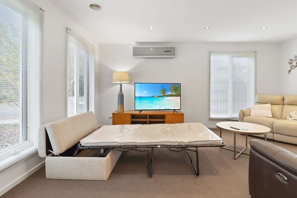 A room with a bed, a television, a sofa, and a lamp.