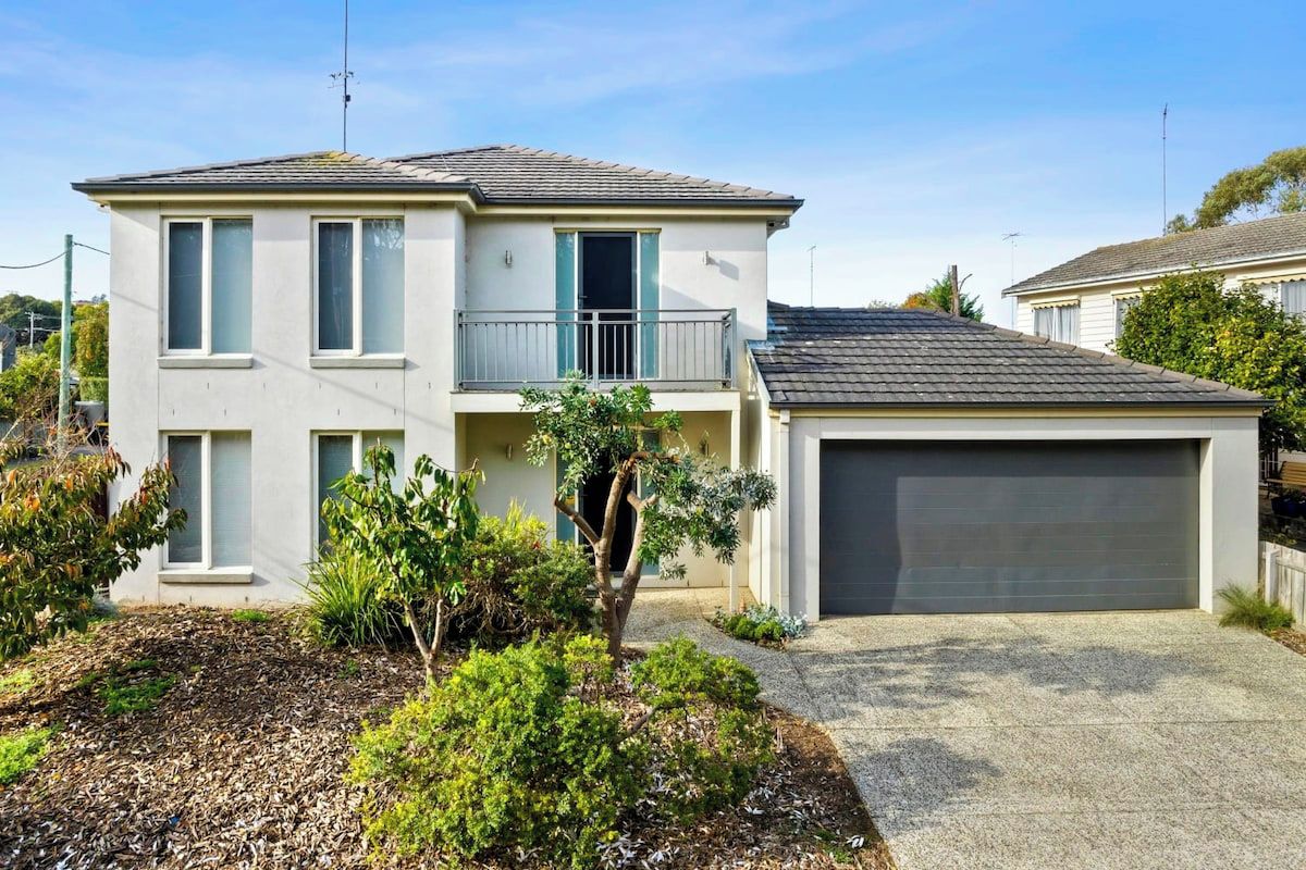 A two-story residential building with a balcony, a garage, and a landscaped front yard.