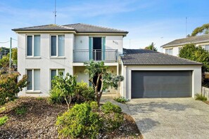 A two-story residential building with a balcony, a garage, and a landscaped front yard.