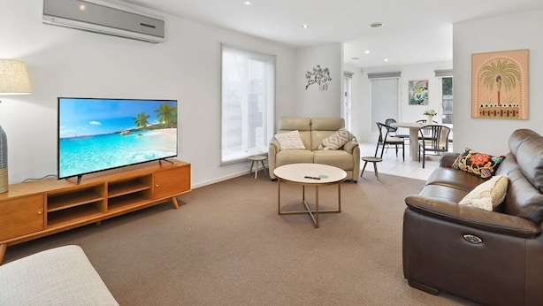 Ein Wohnzimmer mit Flachbildfernseher, einem beigefarbenen Sofa, einem braunen Ledersofa, einem runden Couchtisch und einer Holzwand für Unterhaltungselektronik.