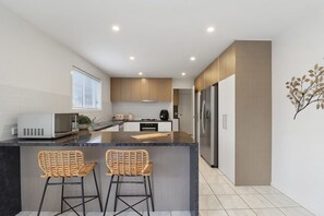 Una cocina moderna con una isla central, dos taburetes de mimbre, electrodomésticos de acero inoxidable y un diseño minimalista.