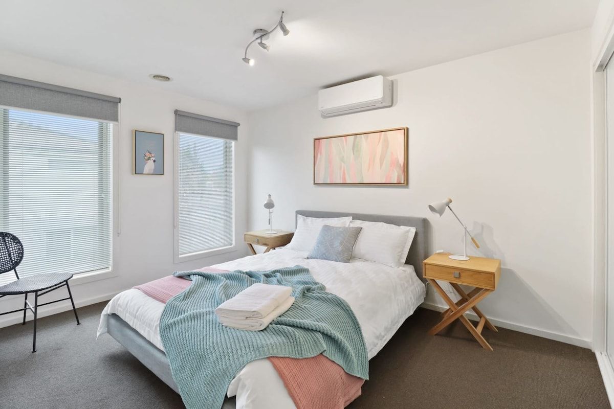 Une chambre à coucher moderne, avec un lit, des tables de chevet, une chaise et des œuvres d’art accrochées aux murs.