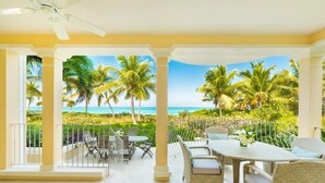 A spacious balcony with a view of the ocean and palm trees, furnished with wicker chairs and a table. - Villa Renaissance 2 Story, 4 Bedrooms, 4 1/2 Baths, Ocean Front Master Bedroom (Grace Bay)