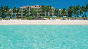 A beachfront hotel with a large building, palm trees, and a clear blue sea. - Villa Renaissance 2 Story, 4 Bedrooms, 4 1/2 Baths, Ocean Front Master Bedroom (Grace Bay)