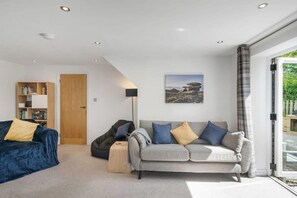 A modern living room with a sofa, a bean bag, a bookshelf, and a door. - Modern Home in Bude, Private Parking & Garden (Bude)