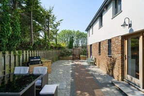 A patio with outdoor furniture, a barbecue grill, and a stone wall. - Modern Home in Bude, Private Parking & Garden (Bude)