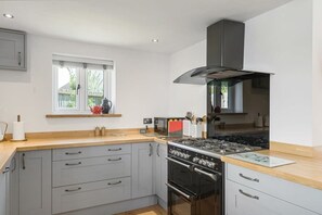 A modern kitchen with grey cabinets, a wooden countertop, a gas stove, and a stainless steel range hood. - Modern Home in Bude, Private Parking & Garden (Bude)