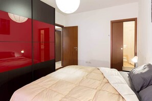 Een moderne slaapkamer met een bed, een rode kledingkast en een houten deur naar een badkamer.