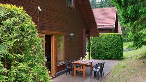 Una casa in legno con patio in mattoni, un tavolo con sedie e un giardino curato.