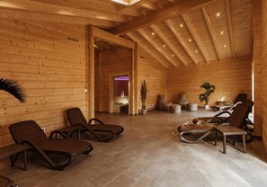 Interior de uma cabana de madeira com poltronas de descanso, mesa de massagem e um pequeno balcão de recepção.