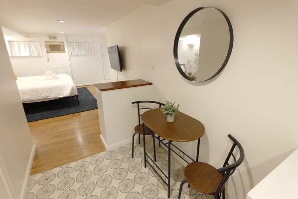 Habitación de hotel con cama, una pequeña mesa con sillas, un espejo y un televisor.