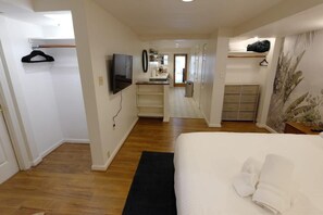 Quarto de hotel com cama, televisão, pequeno espaço de cozinha e banheiro.