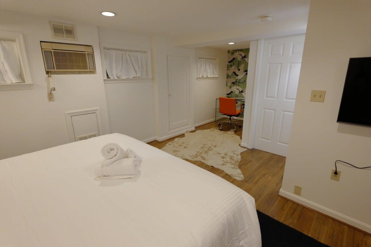 Un dormitorio con cama, una silla, televisor y una puerta que da a otra habitación.