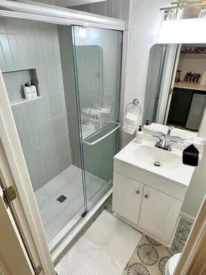 A bathroom with a glass-enclosed shower, a white sink, and a mirror above it.