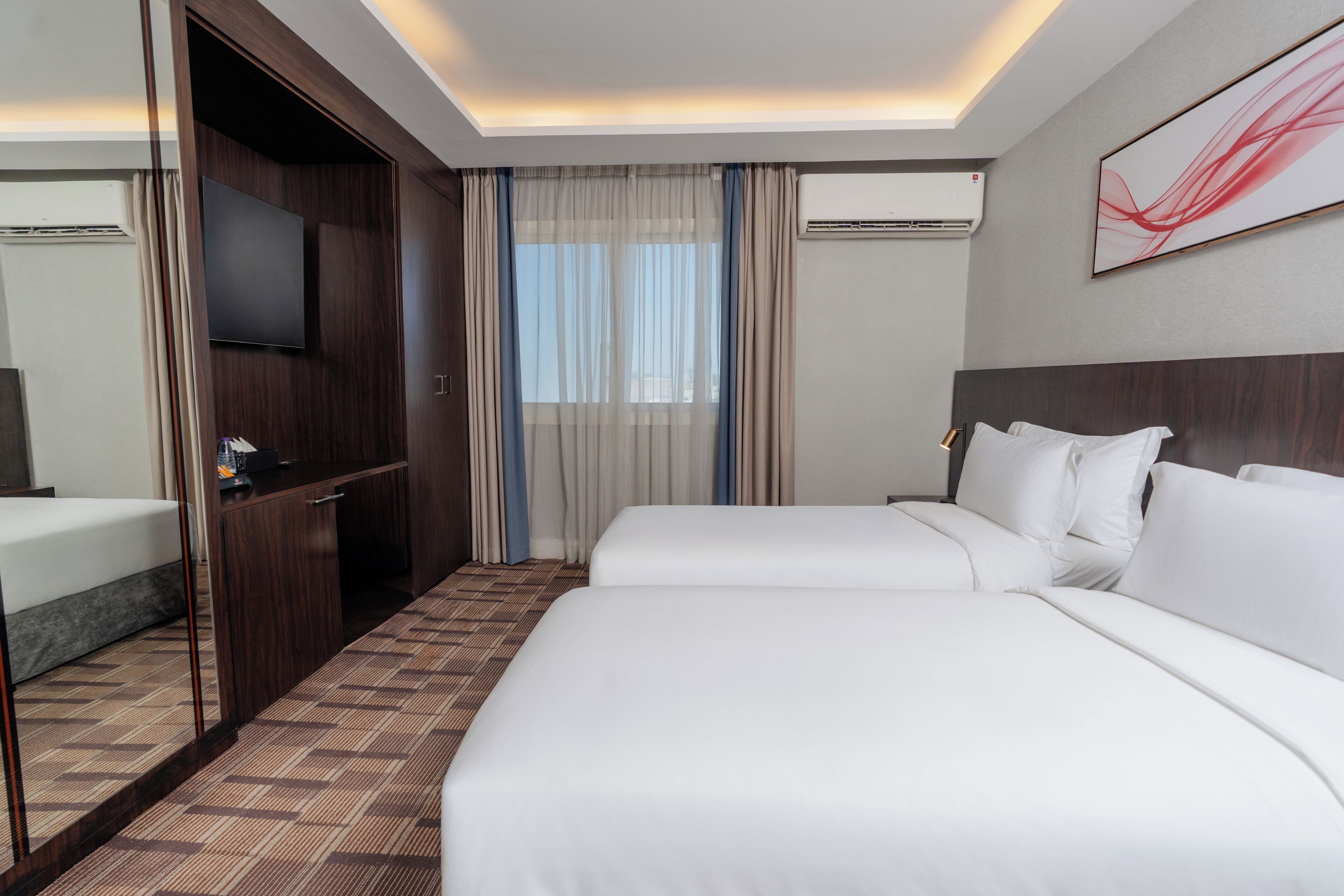 A hotel room with a large bed, a TV, a desk, and a window with curtains.