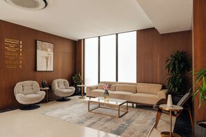 A modern living room with a beige sofa, two armchairs, a coffee table, and a large window. - Howard Johnson by Wyndham Riyadh Al Nasiriyah (Riyadh)