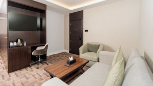 Una habitación de hotel moderna con una televisión de pantalla plana, un escritorio con silla, un sofá y una mesa de centro.