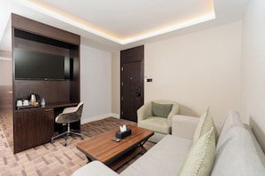 A modern hotel room with a flat-screen TV, a desk with a chair, a sofa, and a coffee table.
