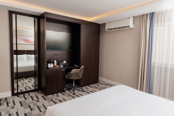 Una habitación de hotel con una cama, un escritorio, una silla, un armario y un equipo de aire acondicionado.