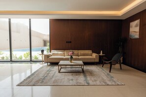 A modern living room with a sofa, coffee table, and a view of an outdoor pool. - Howard Johnson by Wyndham Riyadh Al Nasiriyah (Riyadh)