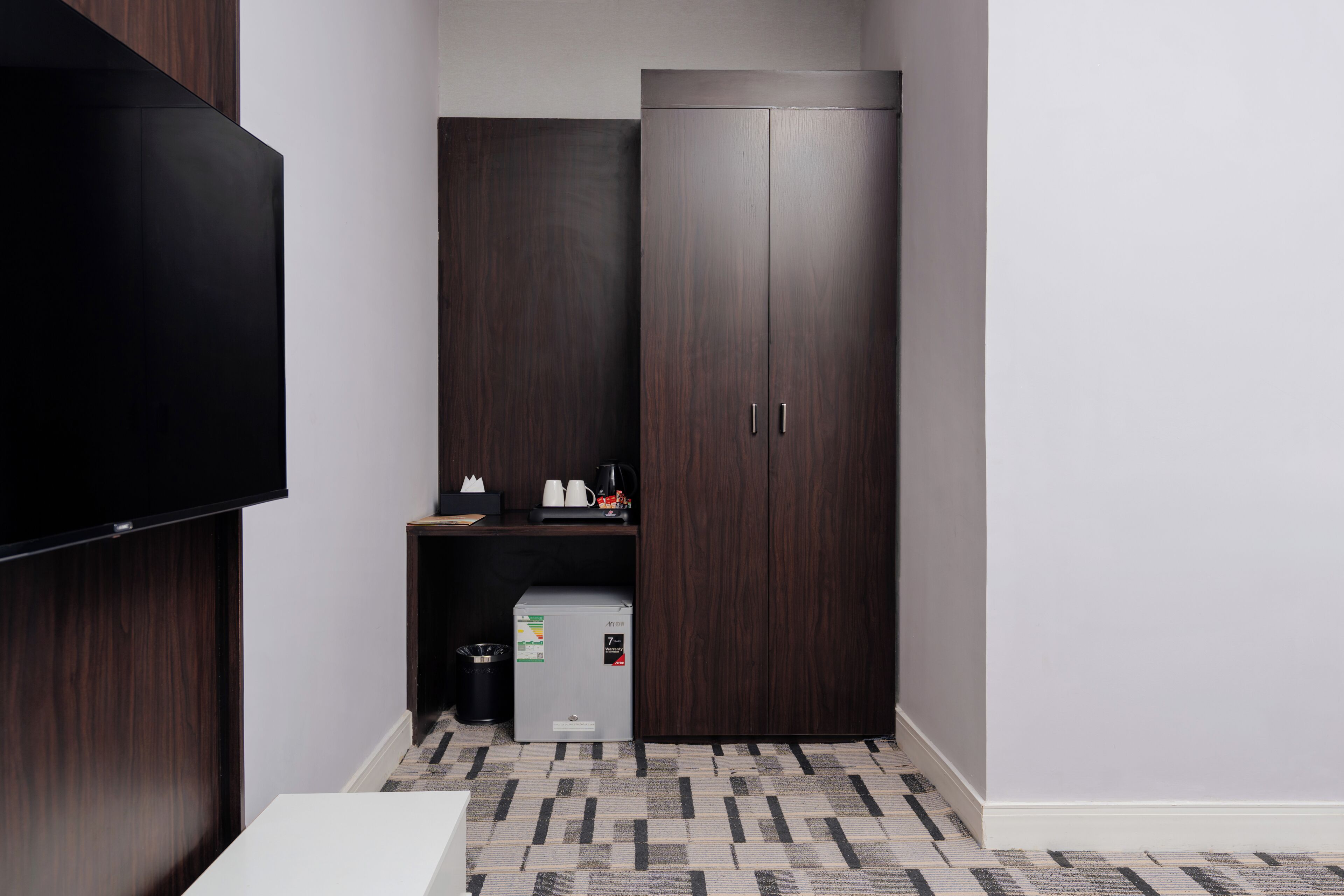 Habitación de hotel con televisión de pantalla plana, minibar, armario y alfombra estampada.