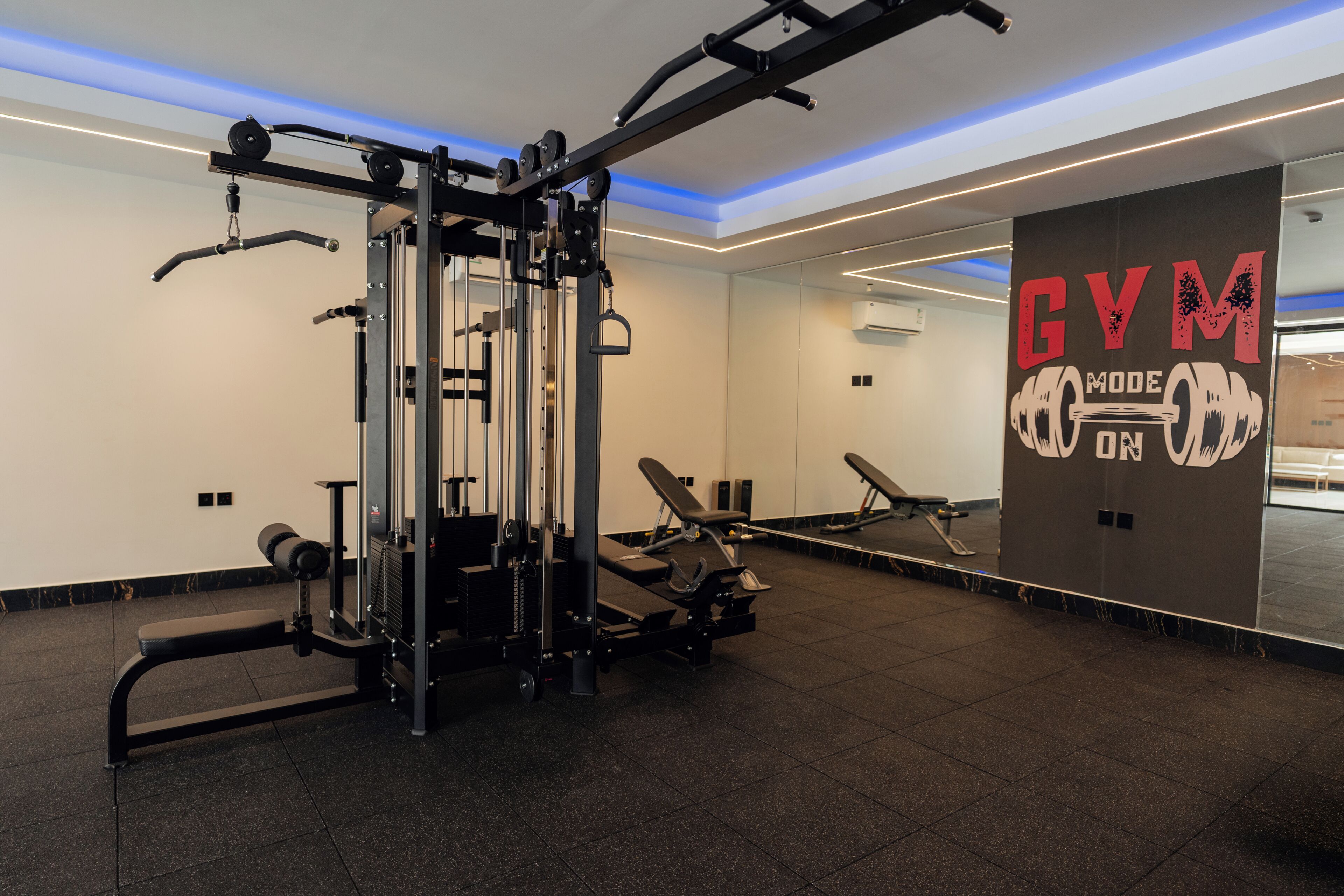 Un gimnasio con equipo de ejercicio, una banca y una pared con la inscripción 'GYM'.