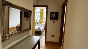 A hallway with a wooden floor, a bench, a mirror, and a door leading to a bedroom with a bed and a window. - 2 bedroom apartment  (London)