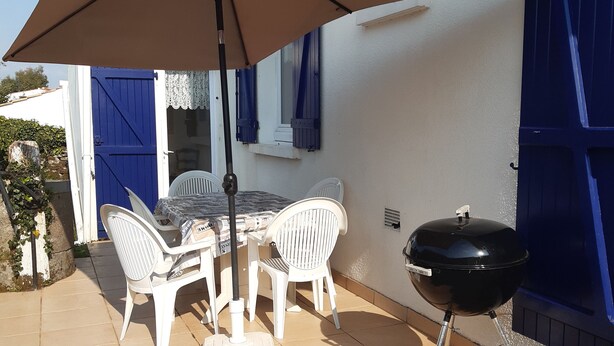 A patio with a table, chairs, a grill, and a striped lounge chair. - Maison 70m2 (L'Épine)