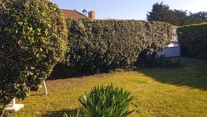 A well-maintained garden with a neatly trimmed hedge, a lawn, and a white lamp post. - Maison 70m2 (L'Épine)