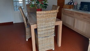 A dining area with wicker chairs and a table, a clock on the wall, and a potted plant with red flowers. - Maison 70m2 (L'Épine)