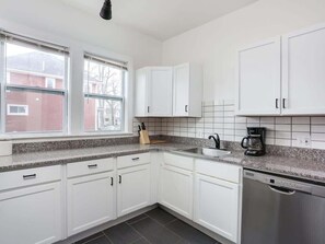 A modern kitchen with white cabinets, a granite countertop, a coffee maker, and a dishwasher. - Comfortable Detroit Home | Parking | Sleeps 12 (Detroit)