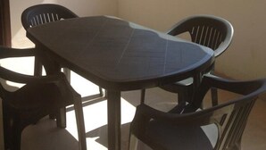 Un balcón con mesa y sillas, un toldo a rayas y vistas a edificios y follaje.