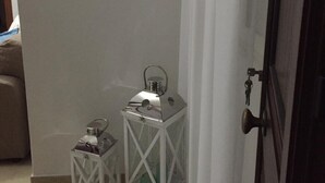 Una habitación con una puerta blanca, un espejo redondo en la pared y dos faroles blancos sobre el suelo.