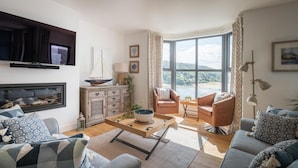A living room with a fireplace, a large window with a view of the beach, and modern furniture. - Blackstone -  stylish apartment with incredible views looking out over the Salcombe estuary (Salcombe)