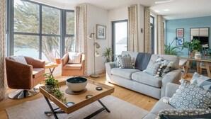 A modern living room with a sofa, armchairs, a coffee table, and large windows with curtains. - Blackstone -  stylish apartment with incredible views looking out over the Salcombe estuary (Salcombe)