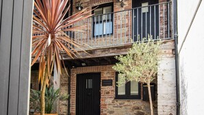 Une cour avec un sol en pierre, un bâtiment en briques doté d’un balcon et des plantes en pot.