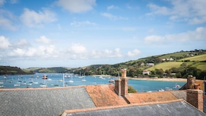 Une vue sur la côte, avec un port rempli de bateaux, une cheminée en briques et une colline parsemée de maisons.