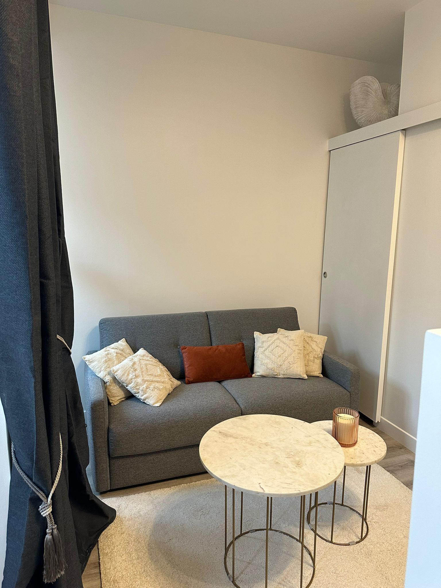 A modern living room with a grey sofa, two round tables, and a black curtain.