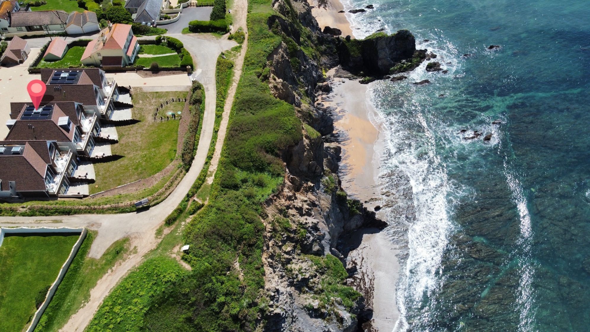 An aerial view of a coastal residential area with houses, a beach, and rocky cliffs.
